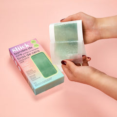 Hand holding a package of wax strips with packaging on a pink background