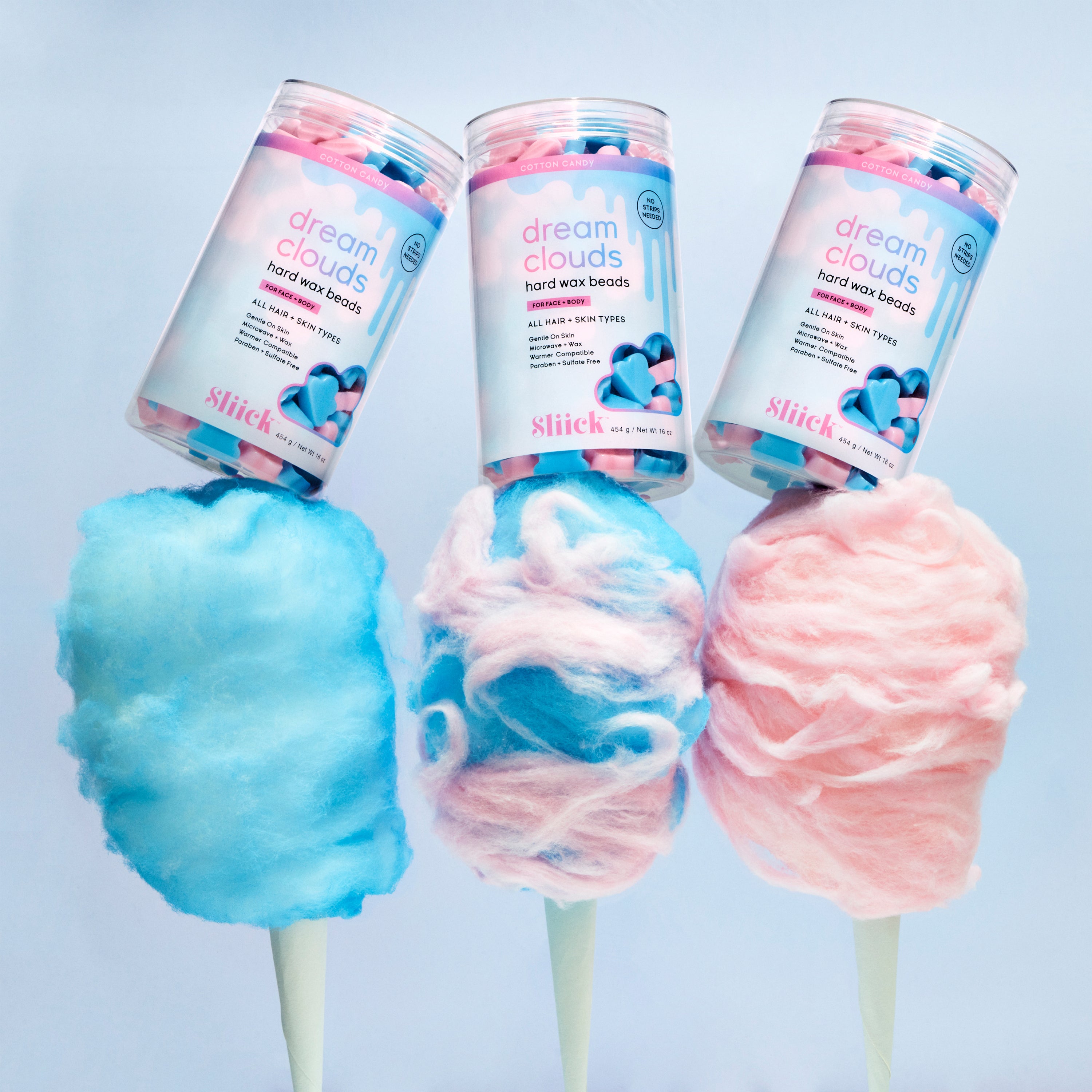 Three containers of Dream Clouds Hard Wax Beads on top of cotton candy on sticks against a light blue background.