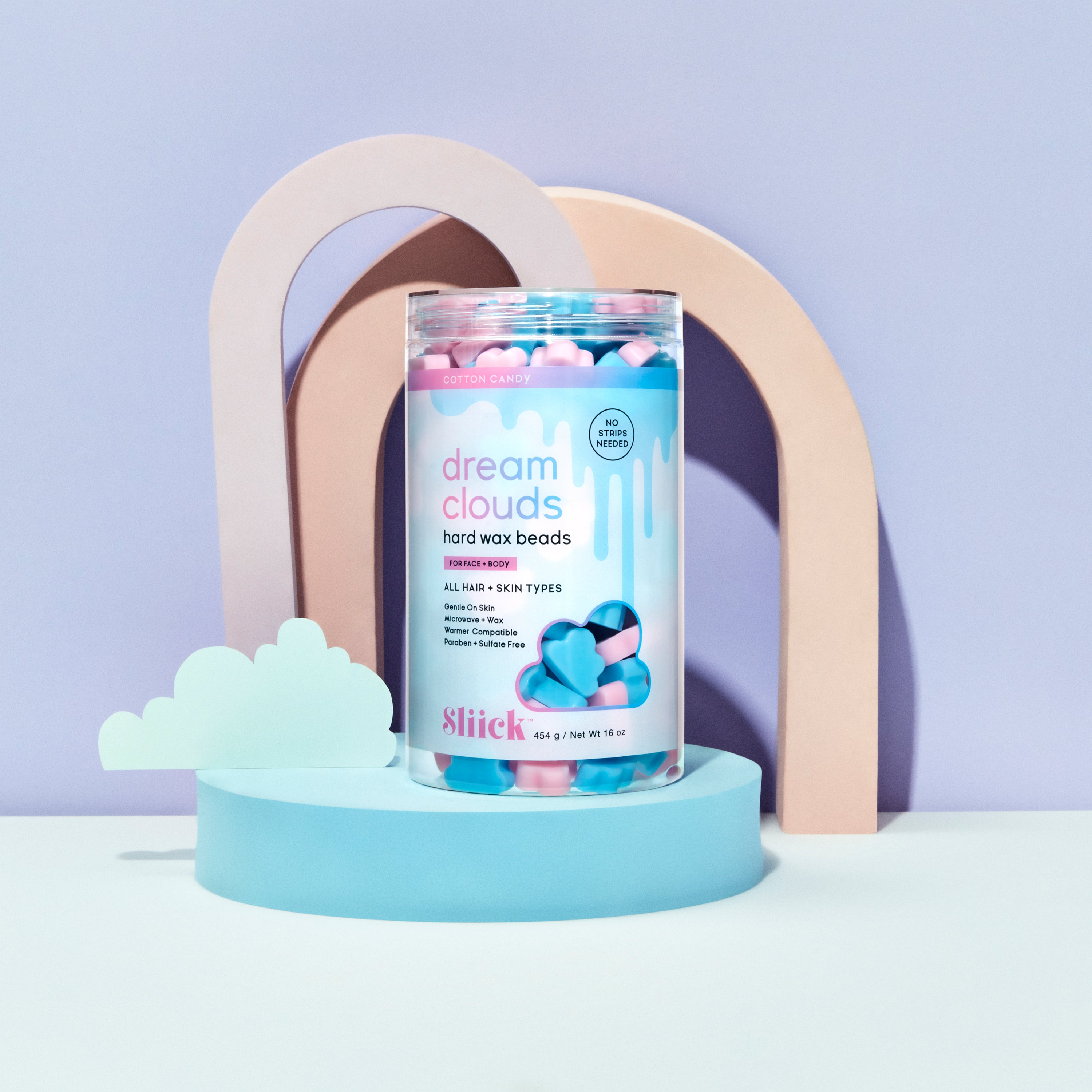 Container of Slick Dream Clouds hard wax beads on a light blue platform with a  stylized pastel arch and cloud decoration in the background.