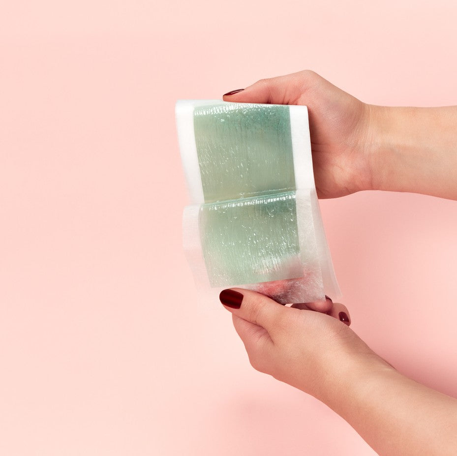 A hand holding a wax strip as display against a pink background