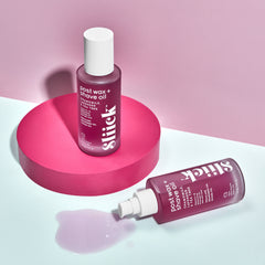 Two bottles of Slick post-wax and shave oil on a pink and white background