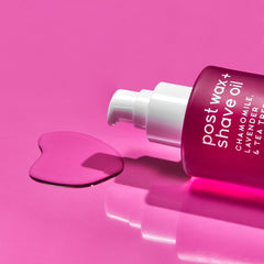 Pink bottle of post wax + shave oil with a droplet on a pink background