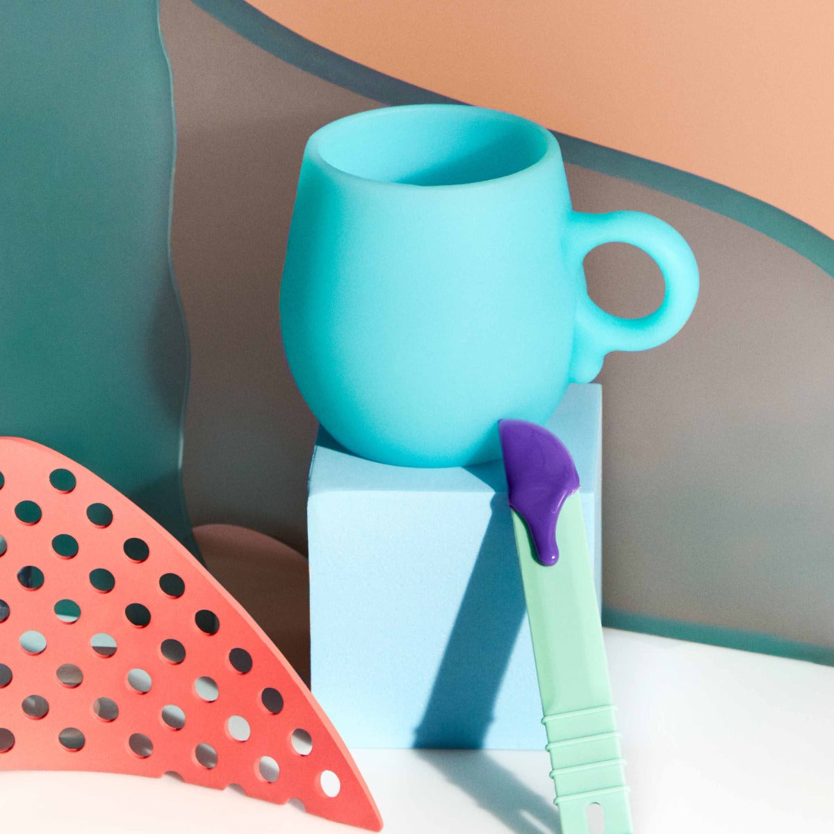 Sliick Silicone Wax Cup – Blue melting cup with a handle & mint spatula with melted purple wax, displayed against a pastel geometric background.