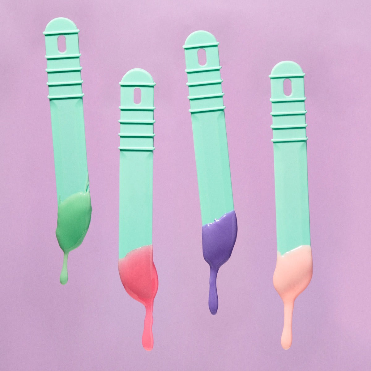 Sliick Hard Wax Beads on Spatulas – Four mint green spatulas dripping colorful wax—green, pink, purple, peach—against a soft lavender background.
